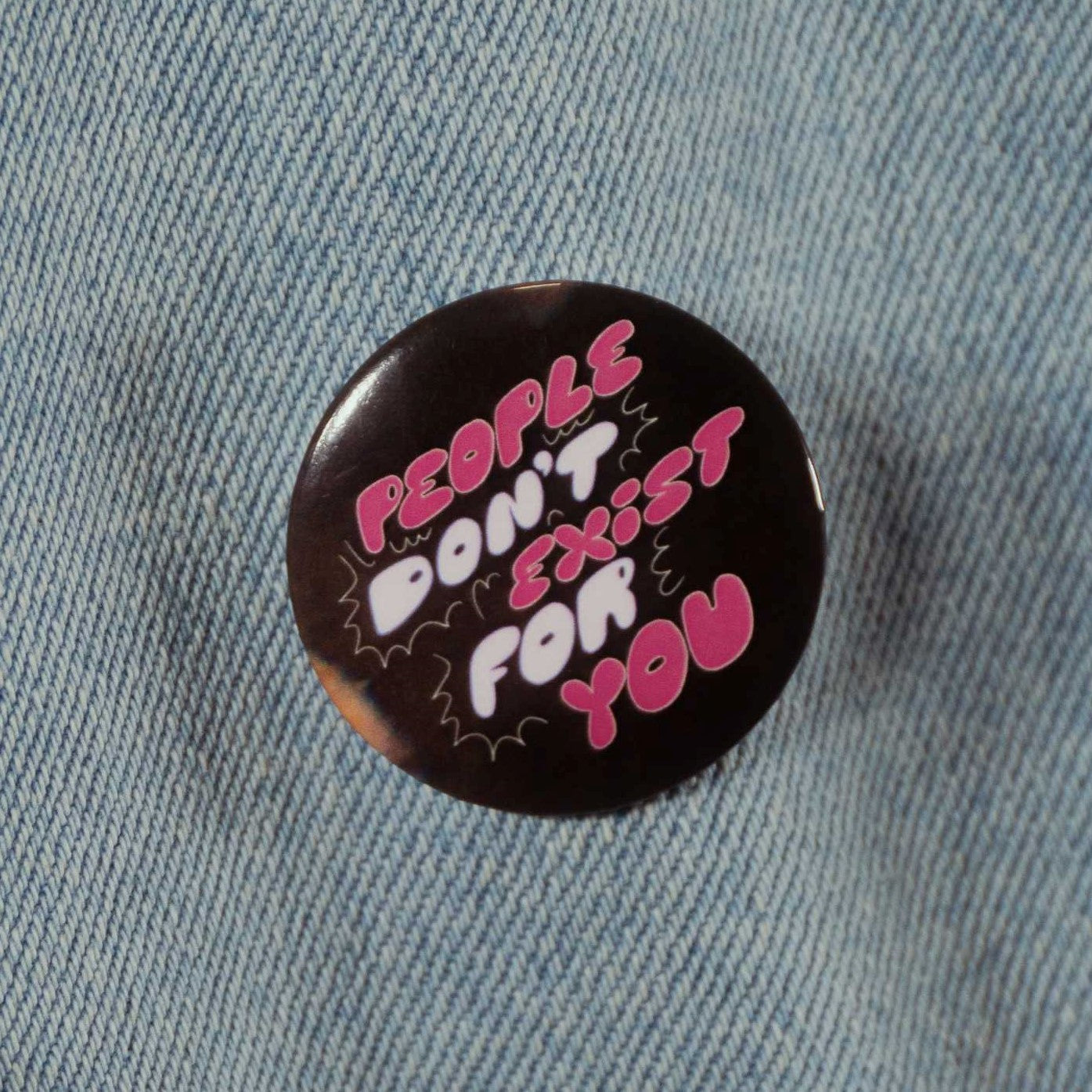 A black circular pin with text that says "people don't exist for you" in pink and white bubble letters.