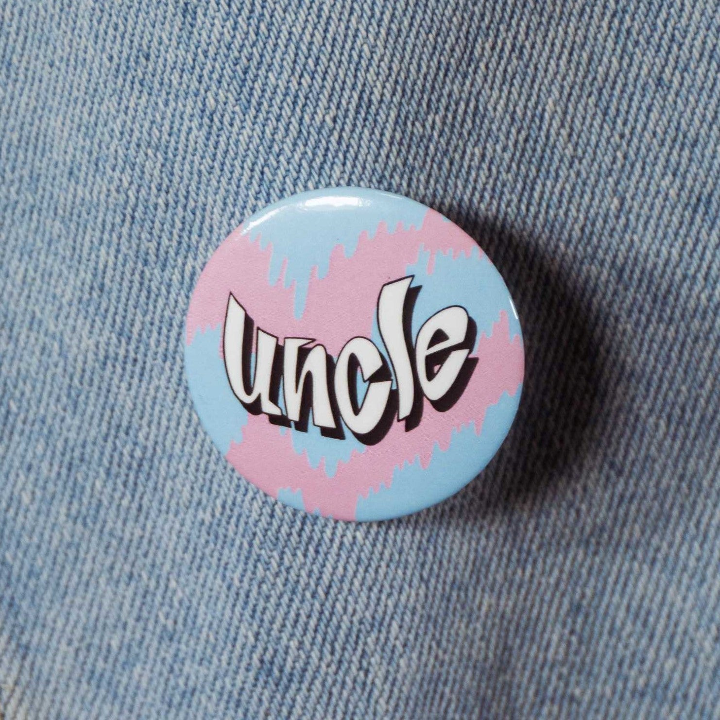 Circular pin with text that says "uncle" with a pastel pink and blue background.