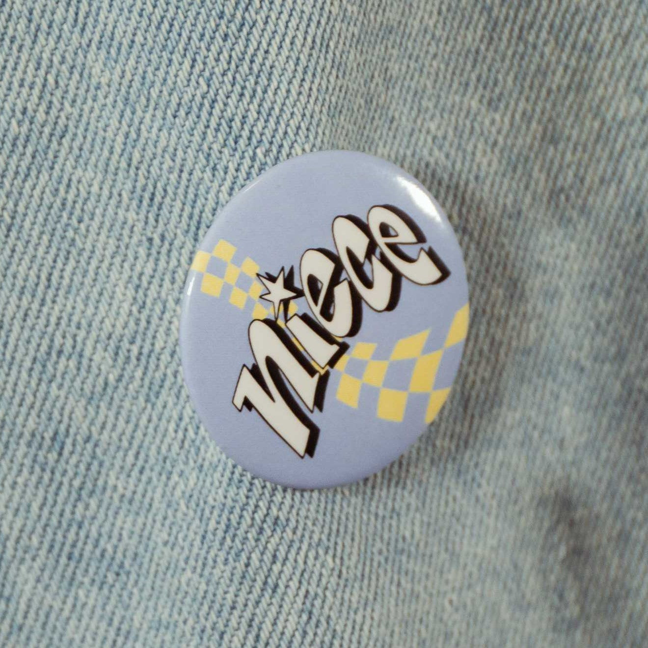 Pastel blue circular pin with text that says "niece" with a yellow checkered background.