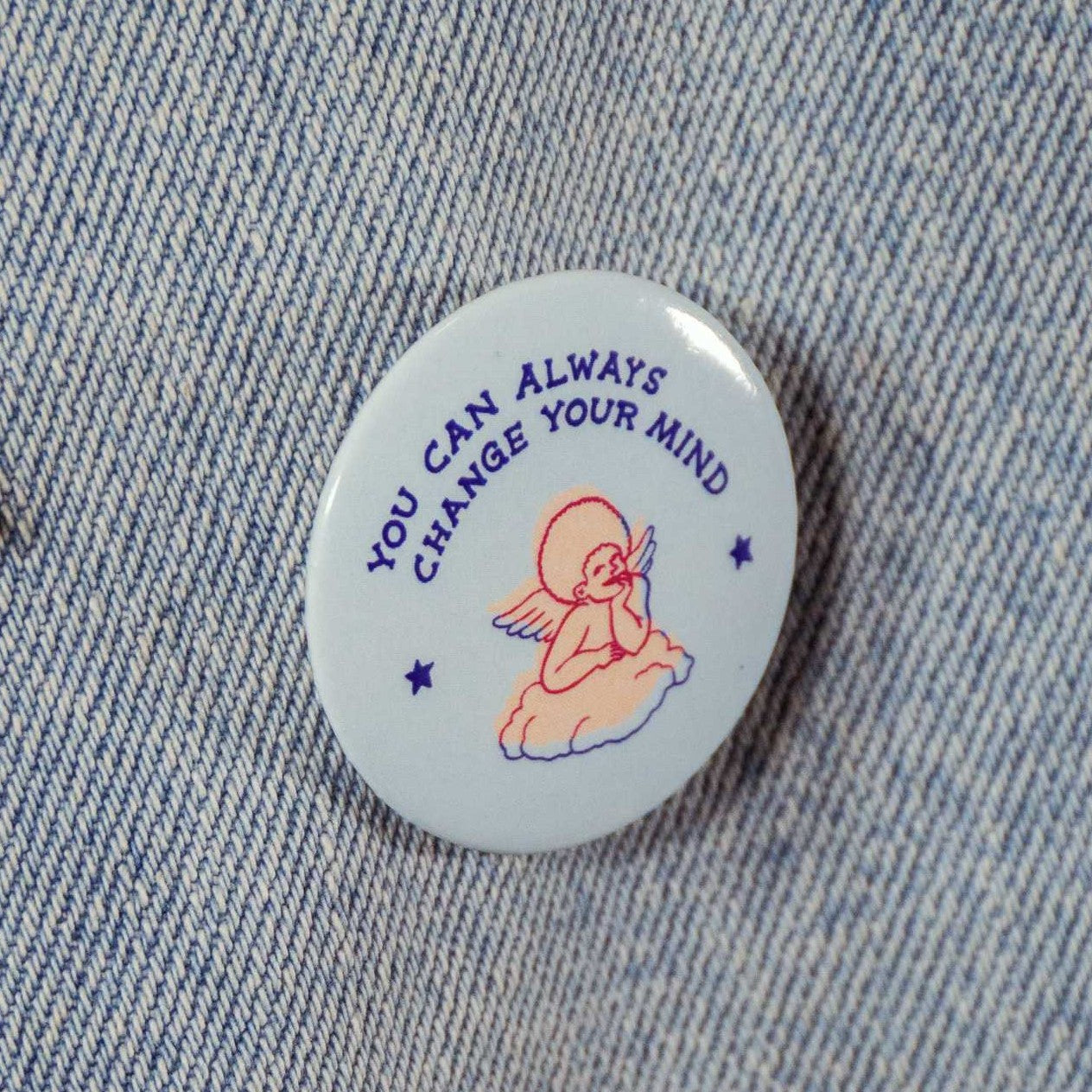 Pastel blue circular pin with text that says "you can always change your mind" with an image of a pastel pink, hand-drawn angel .