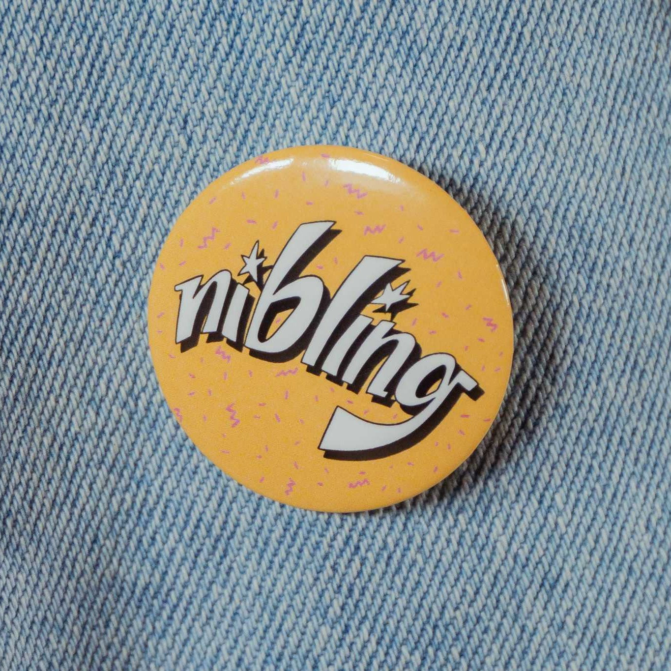 An orange circular pin with text that says "nibling" with purple squiggles in the background..