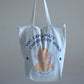 White canvas tote bag with writing that says "you can always change your mind" in dark-blue text, with a hand-drawn image of a pastel-pink angel.