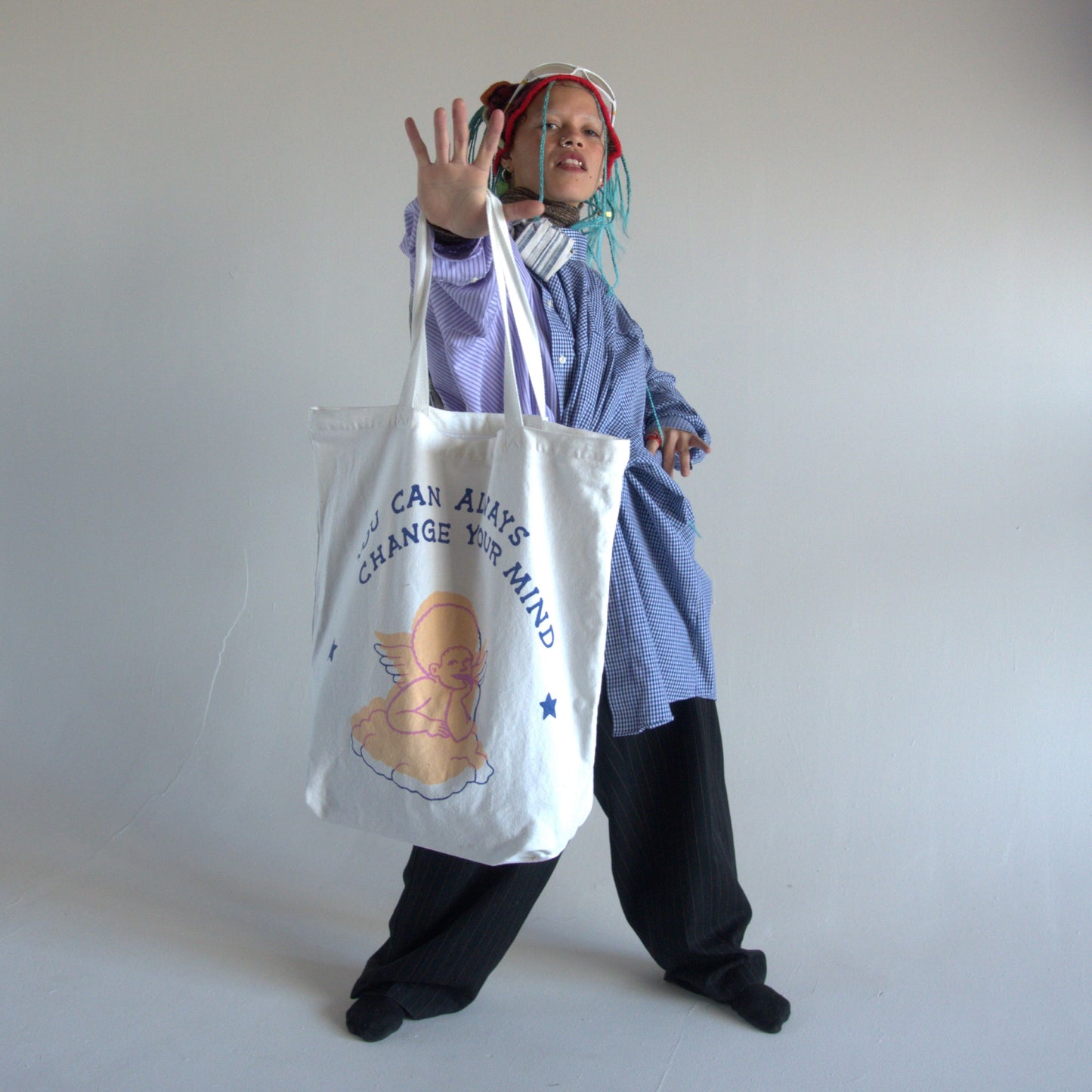 White canvas tote bag with writing that says "you can always change your mind" in dark-blue text, with a hand-drawn image of a pastel-pink angel.